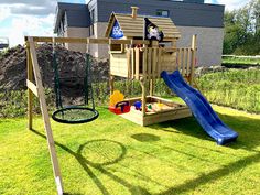 a wooden swing set with a blue slide in the grass next to a house and yard