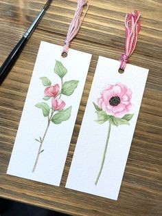 two tags with watercolor flowers on them sitting on a table next to a pair of scissors