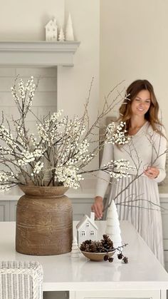 a woman standing next to a kitchen counter with flowers in a vase on top of it