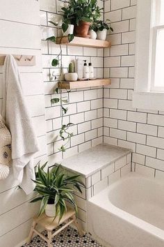 a white tiled bathroom with plants and towels on the shelf next to the bathtub