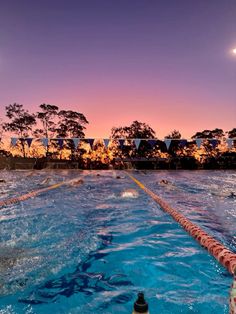 an empty swimming pool at dusk with people in the water and flags flying above it