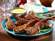 lamb chops are served on a blue plate with dipping sauce and wine glasses in the background