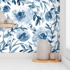 a white vase sitting on top of a counter next to a wallpaper covered in blue flowers