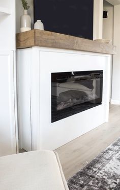 a living room with a white fireplace and black screen on the wall over the fire place