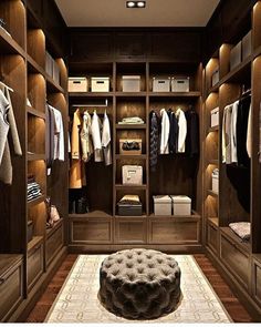 a large walk in closet with lots of clothes on the shelves and an ottoman underneath