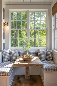 a wooden table sitting under a window next to a bench with pillows on top of it