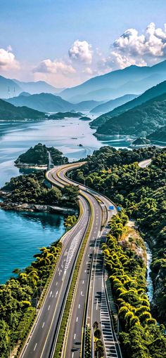 an aerial view of a highway going through the mountains and into the water with trees on both sides