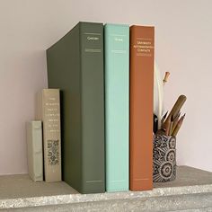 three books are sitting on a shelf next to a pen and pencil holder with pens