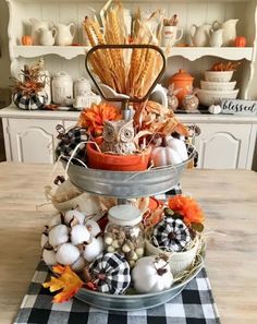 a three tiered tray with pumpkins and gourds in it on top of a table