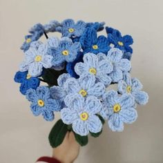 a crocheted blue and yellow flower bouquet in someone's hand on a white background