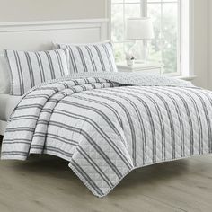 a bed in a bedroom with white walls and wooden floors, along with a striped comforter set