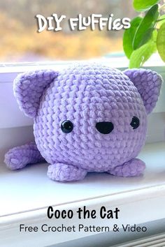 a purple crochet cat sitting on top of a window sill next to a plant