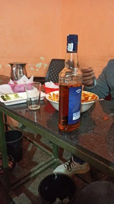 a man sitting at a table in front of a bottle of alcohol and some glasses