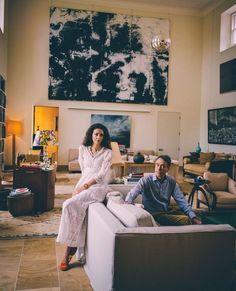 a man and woman sitting on couches in a living room with paintings above them