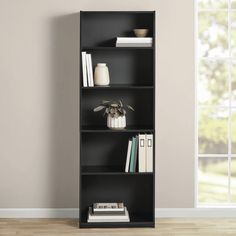 a black bookcase with four shelves in front of a white wall and wooden floor