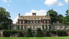 a large red brick building sitting in the middle of a lush green field next to trees