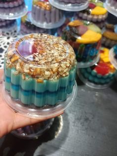 a hand holding a cupcake with blue icing and nuts on top in front of other cupcakes