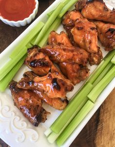 chicken wings and celery on a white plate with ketchup in the background