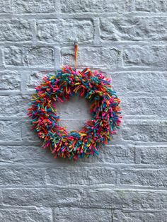 a wreath made out of sprinkles hanging on a brick wall with a string