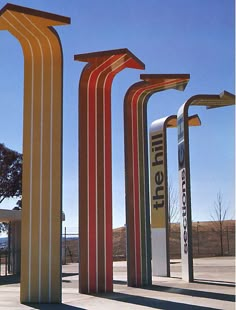 three tall metal sculptures sitting in the middle of a parking lot next to a tree