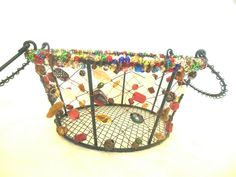 there is a wire basket with beads on the bottom and chains hanging from it's sides