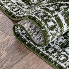 a green and white area rug on the floor with wood floors in the back ground