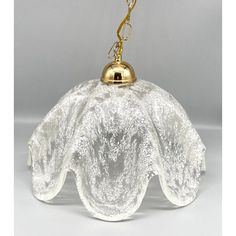 a glass light hanging from a chain on a white surface with a gold ball in the middle