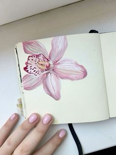 a woman's hand holding an open notebook with pink flowers on it