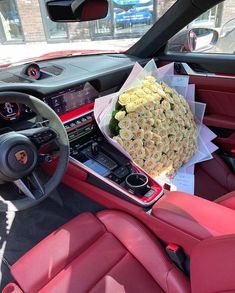 a bouquet of roses is sitting in the center console of a red sports car, next to a steering wheel