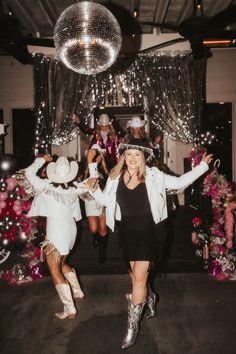 two women in cowboy hats and boots are dancing with disco balls hanging from the ceiling