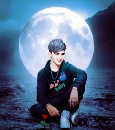 a young man sitting on the ground in front of a full moon with his hands crossed