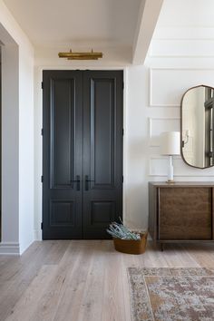 a black door in a white room next to a brown cabinet and mirror on the wall