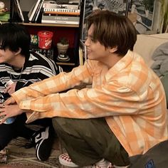 two young men sitting next to each other on the floor in front of a book shelf