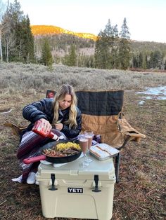 a woman sitting in a chair next to a cooler with food on top of it