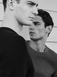 two young men standing next to each other in front of a white house, one looking at the camera