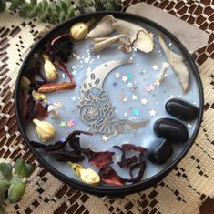 a bowl filled with rocks and flowers on top of a lace covered table cloth next to a plant