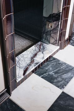 a bathroom with black and white tiles on the floor, shower stall door and mirror