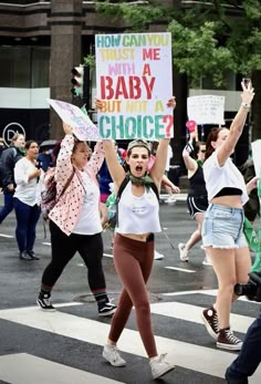 two women holding signs in the middle of a crosswalk with other people walking behind them