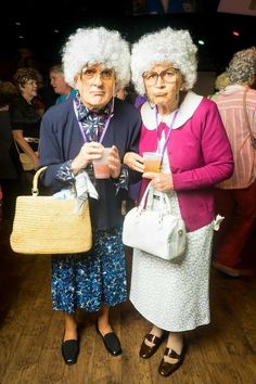 two older women standing next to each other holding purses and looking at the camera