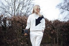 a woman walking down the street in white pants and a black sweater with an arrow on it