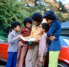 a group of people standing next to each other in front of a red car on the street