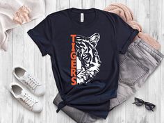 An awesome shirt for any Tigers' Fan! Choose your favorite shirt color and customize the tiger and font with your team's color *Other shirt colors may be available, send us a message if you are looking for something specific * Bella+Canvas3001 Unisex Style Shirt - A classic unisex jersey short sleeve tee. - Solid colors are 100% cotton   Ash is 99% cotton and 1% polyester Heather colors and Solid Black Blend are 52% cotton, 48% polyester  - Athletic Heather and Black Heather are 90% cotton, 10% Tiger Tshirt, Shirt Graphic Design, Game Day Football, Tiger Shirt, Style Shirt, Football Shirt, Unisex Style, Favorite Shirts, Team Colors