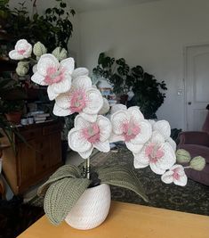 a white vase with pink flowers sitting on a table in front of a couch and potted plant