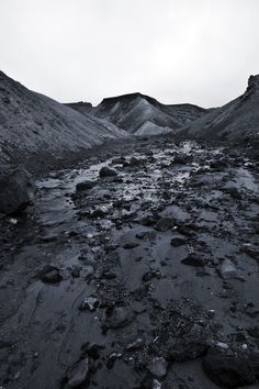 a black and white photo of rocks and water in the desert with mountains in the background