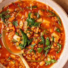 a white bowl filled with beans and greens on top of a wooden table next to a spoon