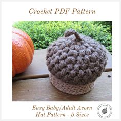 the crochet baby hat is sitting on a wooden table next to an orange pumpkin