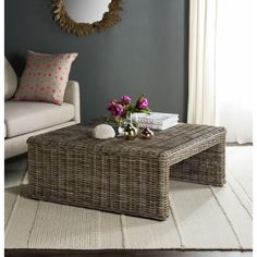 a wicker coffee table with flowers on it in front of a couch and mirror