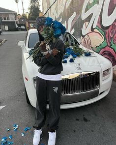 a man standing in front of a white car with flowers on the hood and head