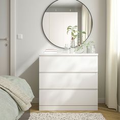 a white dresser sitting next to a bed under a round mirror