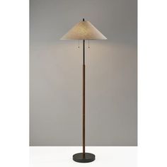 a floor lamp with a white shade on the top and a black base, in front of a gray wall